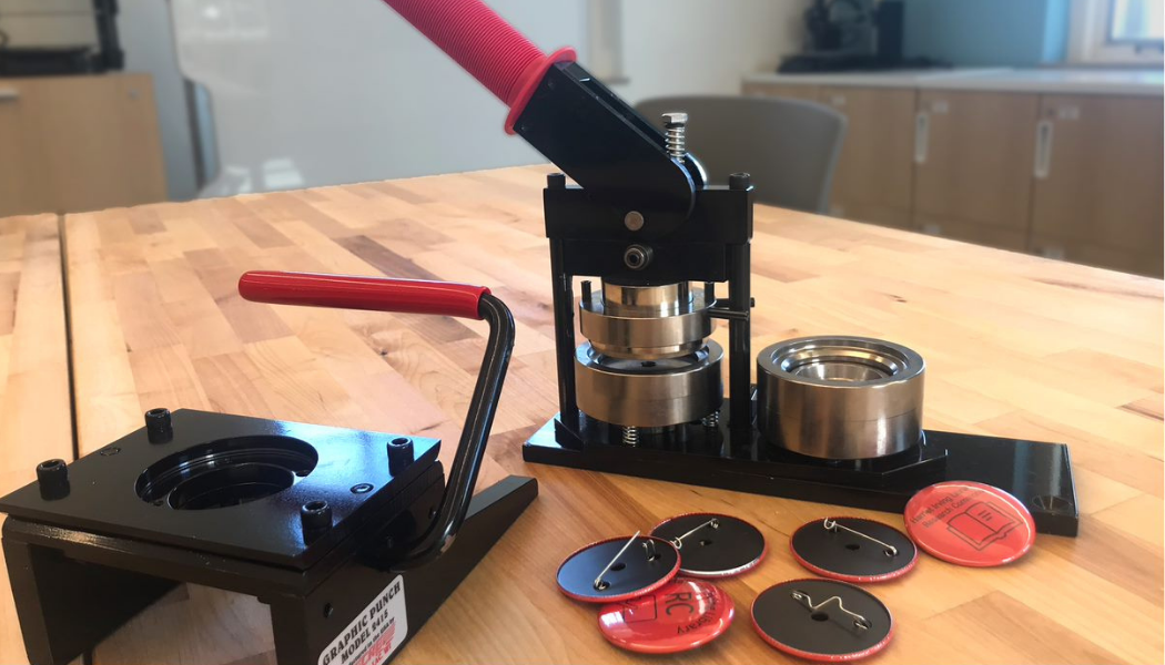 An image of the Fabrication Lab Button Maker, with example buttons for reference. 