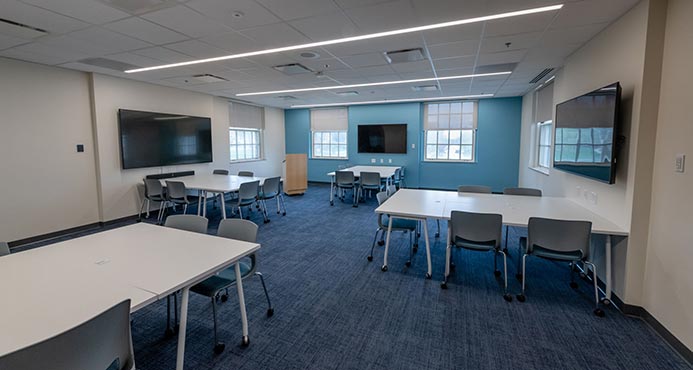 A view of the active learning space's work pods and wall-mounted 55-inch LCD screen