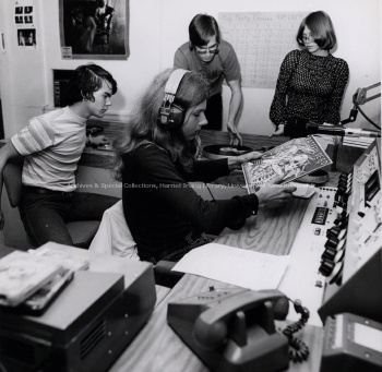 Fredericton High School students Dave Clarke (with headset), Anne McKay and Kevin Hastings (seated left) learn about on-air broadcasting techniques from summer program director Maurice Latouche (adjusting record), 1974. PR; Series 1; Sub-series 7; Item 7750.