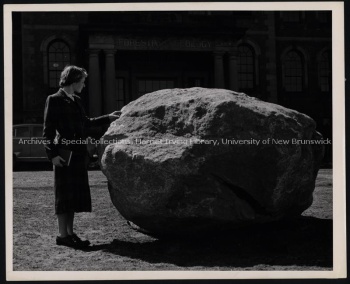 Woman standing beside the glacial boulder in front of Forestry and Geology Building. UA PC-12 no. 1.