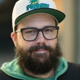 Photo of Mike Nason. He has glasses and a beard, and is wearing a hat that says "Fridays". 